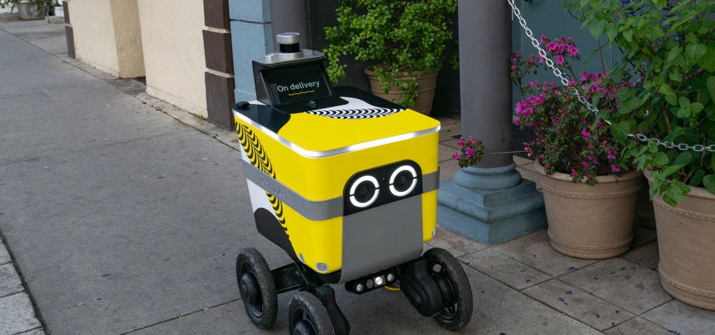 A photo of a Postmates food delivery robot going down a sidewalk.