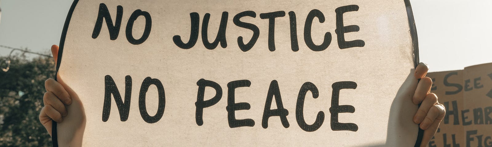 At a protest, a person holds a white sign that says, “No justice, no peace.”