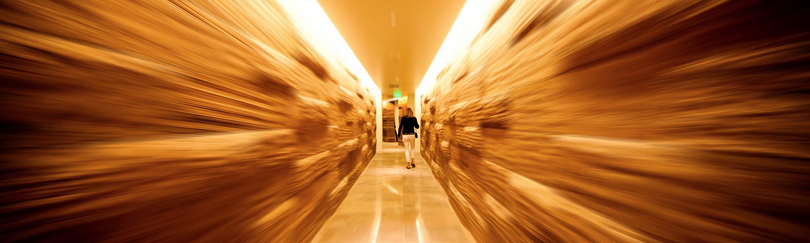 A blurred image of an aisle in a grocery store, focused on the center where a woman is walking.