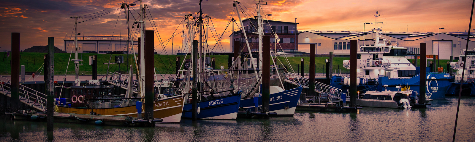 A line of fishing boats waiting in a harbour at sunset.