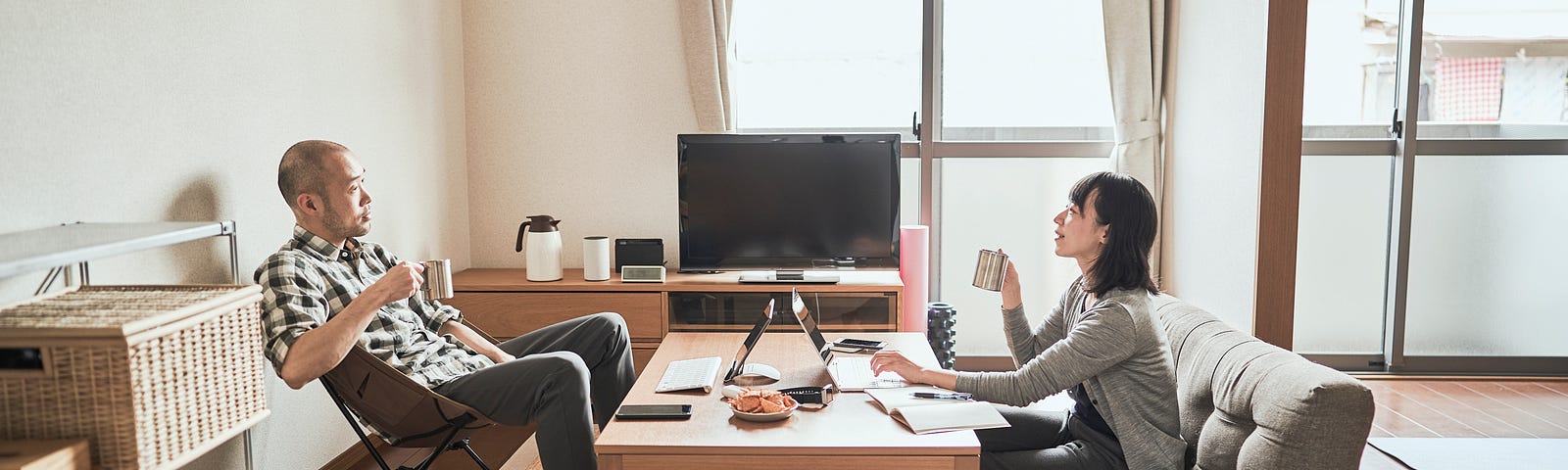 A couple sits on opposite sides of a coffee table, working on their laptops together at home.