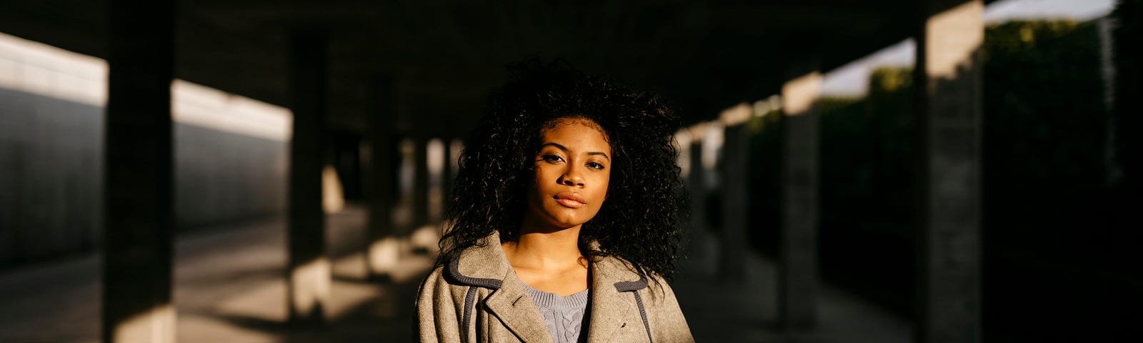 A Black woman standing in a dim parking garage with the light shining on her.