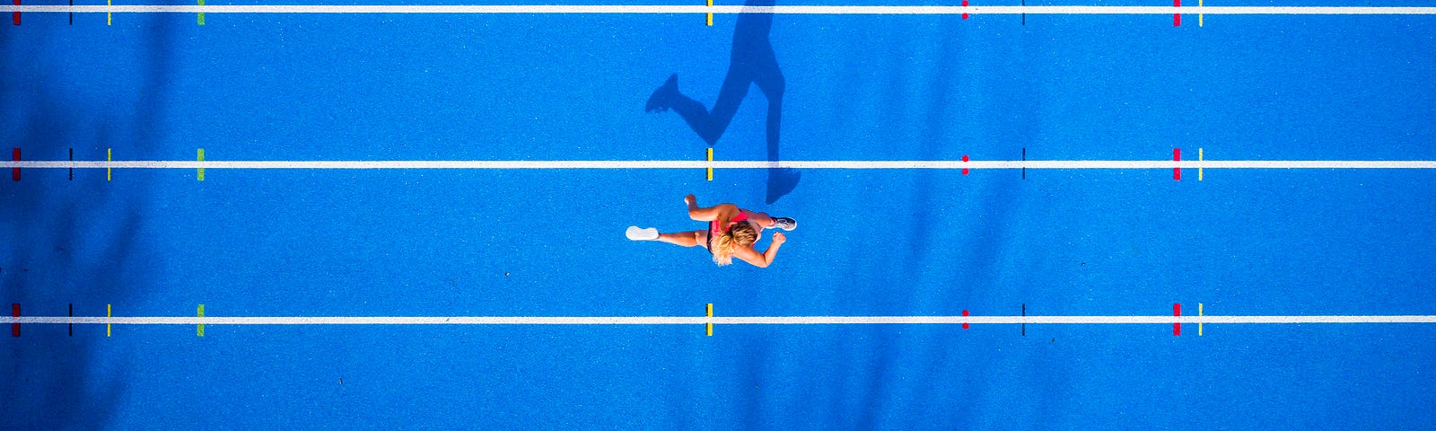 An aerial photo of a person running on a track. Their shadow looks like it’s running.