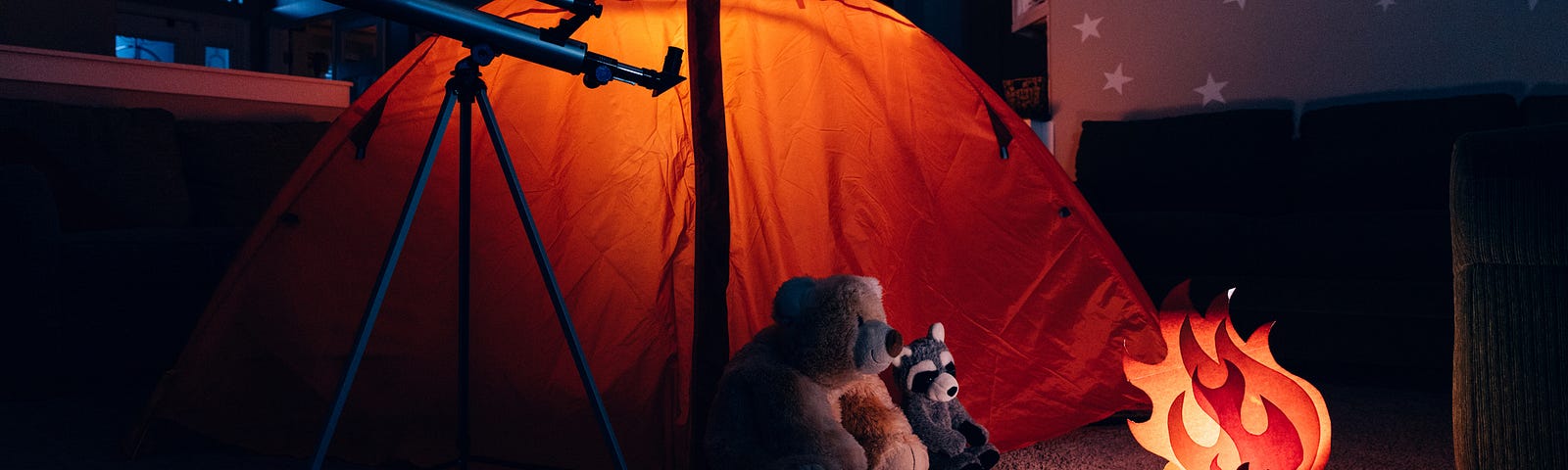 Tent and fake campfire set up indoors with stuffed animals huddled around the fire and a telescope.