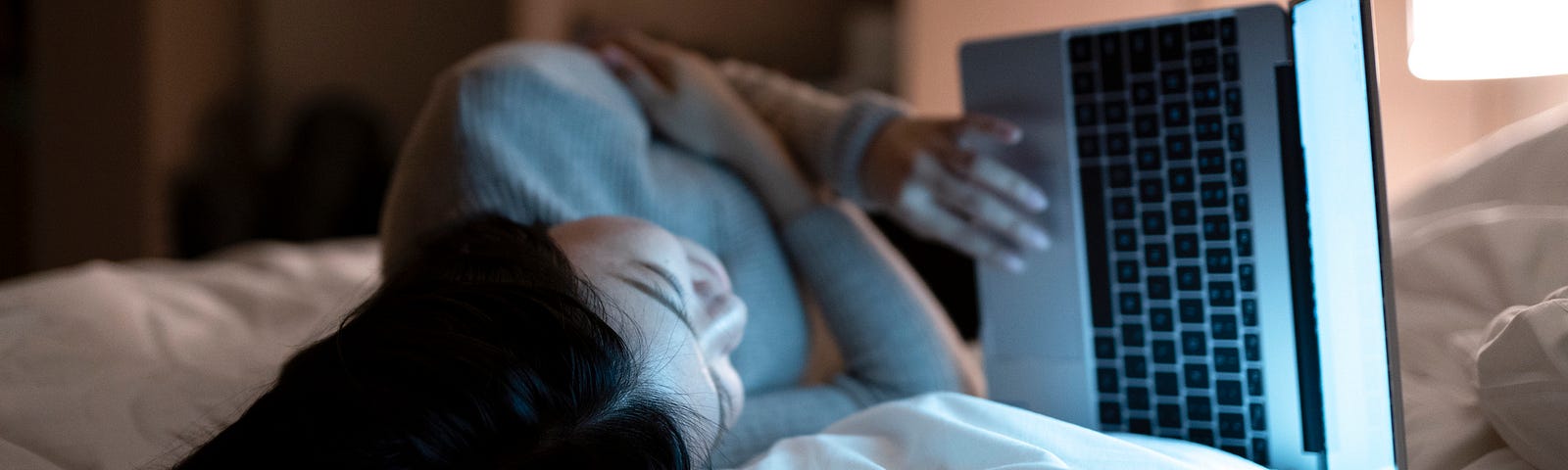 A photo of a woman on her laptop, lying in bed.