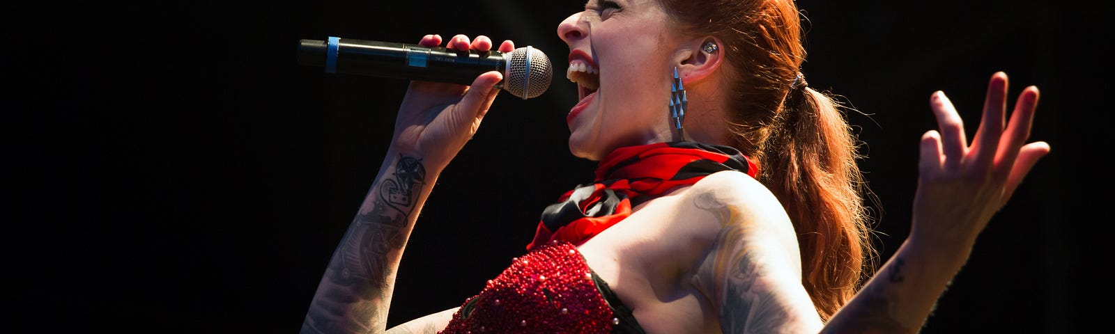 Female singer with long red hair wearing a strapless red dress belting out a song on stage