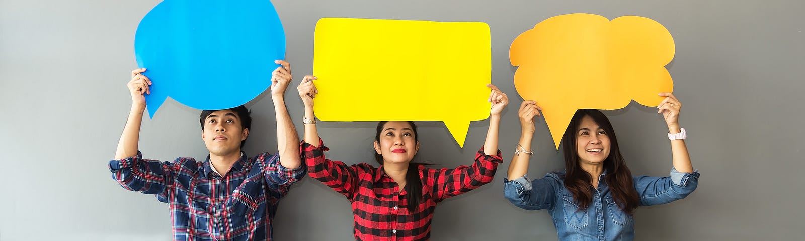 A man and two women sit on the floor holding cut out speech bubbles over their head.