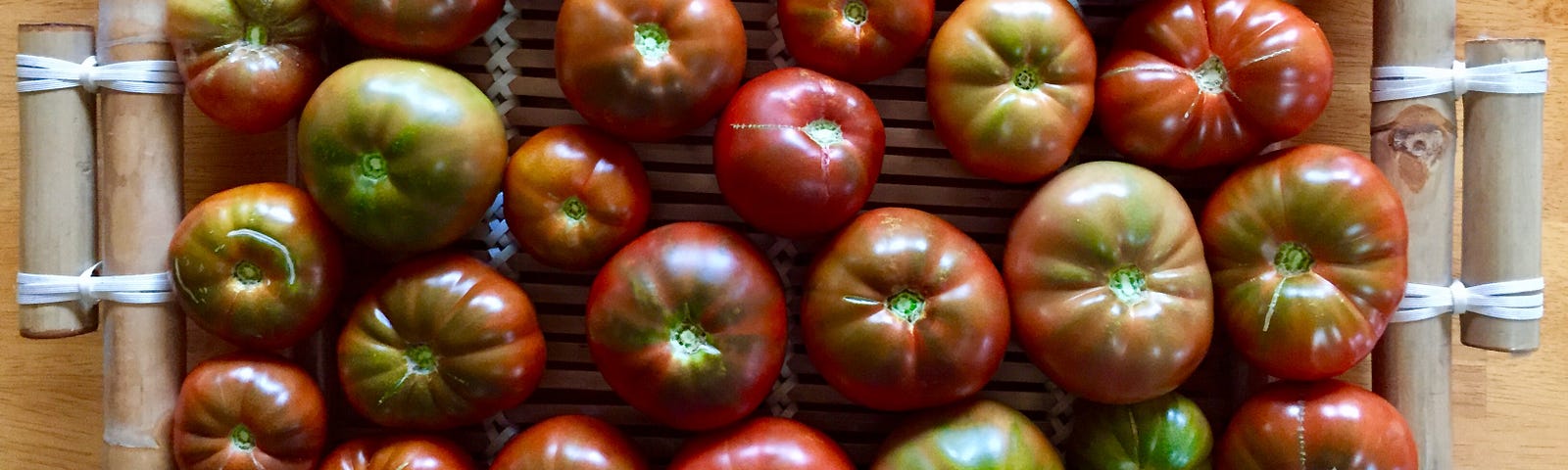 Aerial view of a shallow bamboo tray filled with a single layer of red/brown/green heirloom tomatoes.