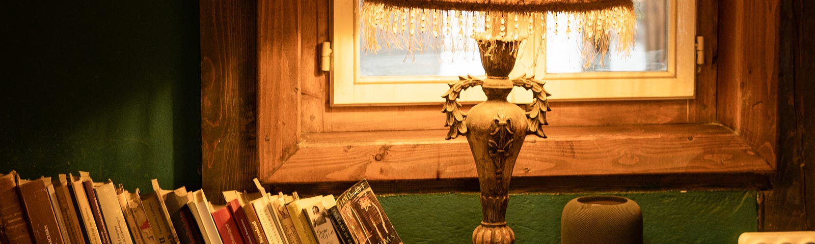 A bookshelf with a lighted lamp on it, with a window in the background.