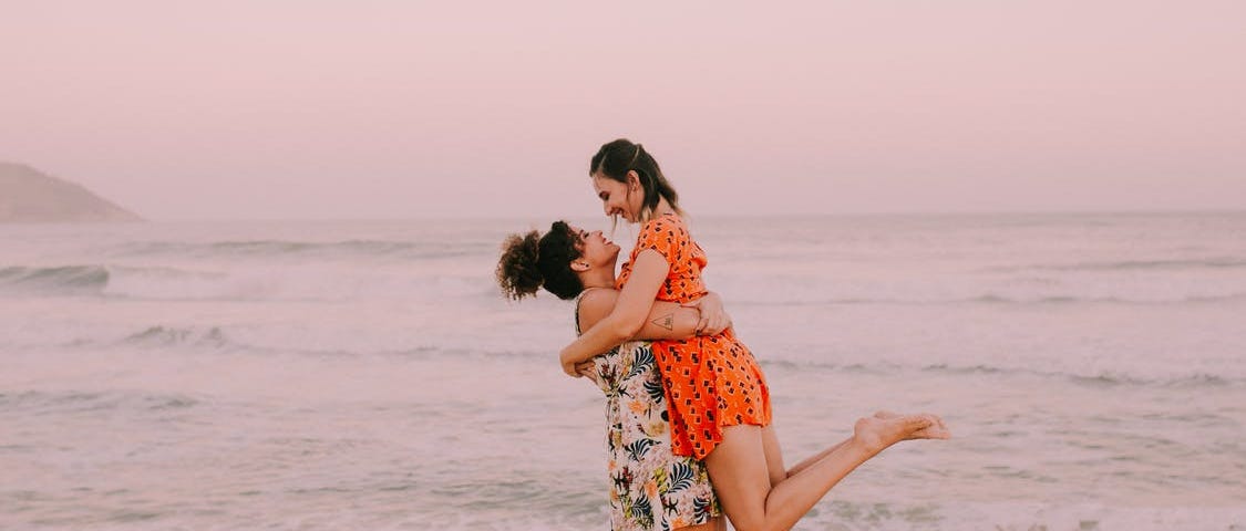 A woman picked up her partner on the beach. Both are smiling. The sunset is pink behind them. #relationships #dating #love