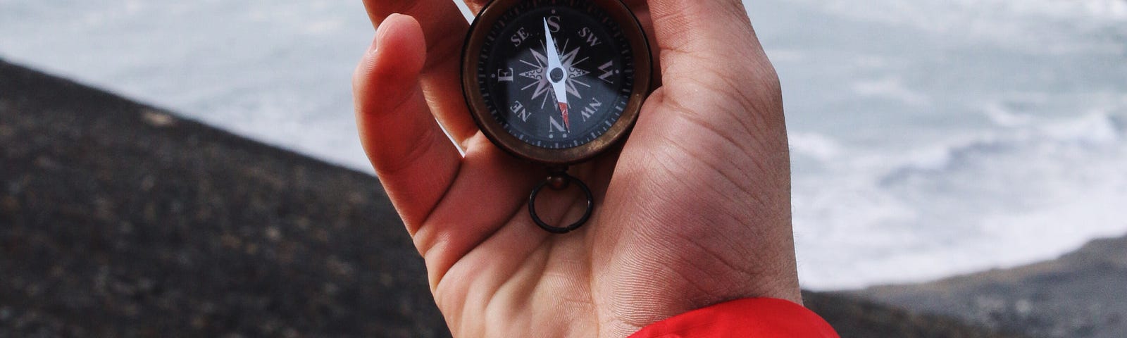 a hand holding a compass along a shoreline