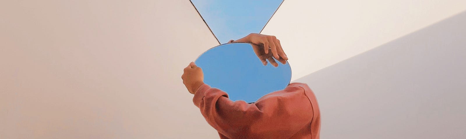 A photo of a person holding a mirror that reflects the blue sky. The mirror is covering their face.
