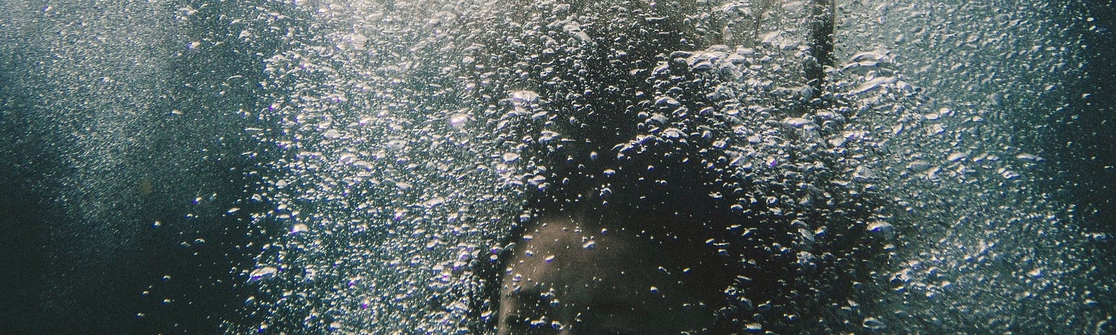 A photo of a woman submerged underwater, with a ton of water bubbles.