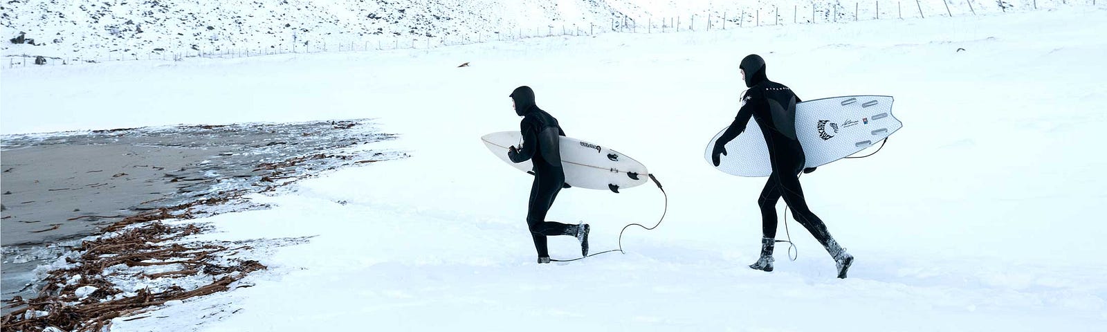 Surfers run across the snow toward Unstad beach in Norway.