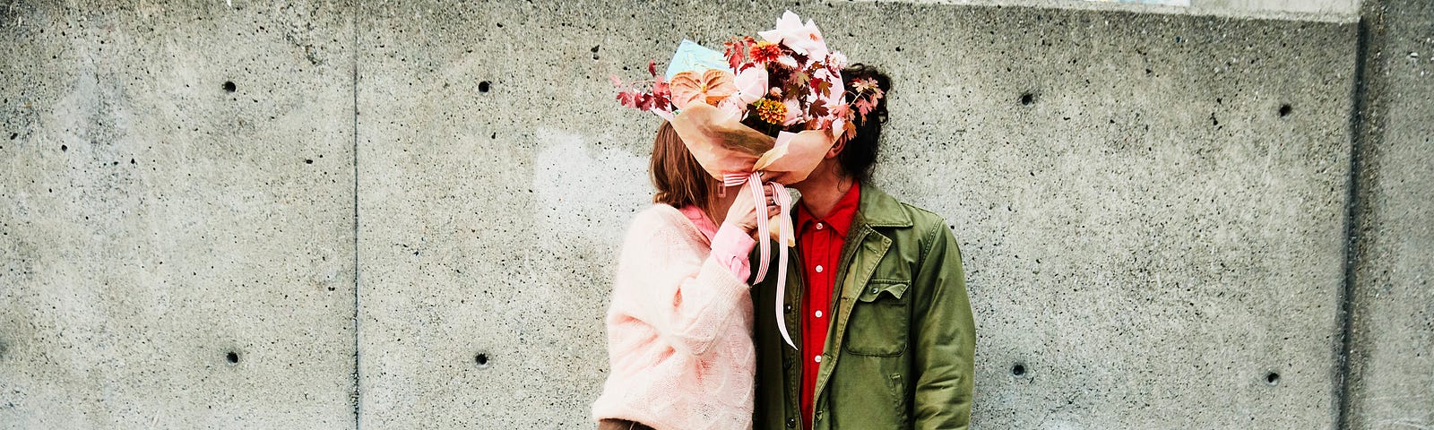 Couple kissing behind bouquet of flowers.