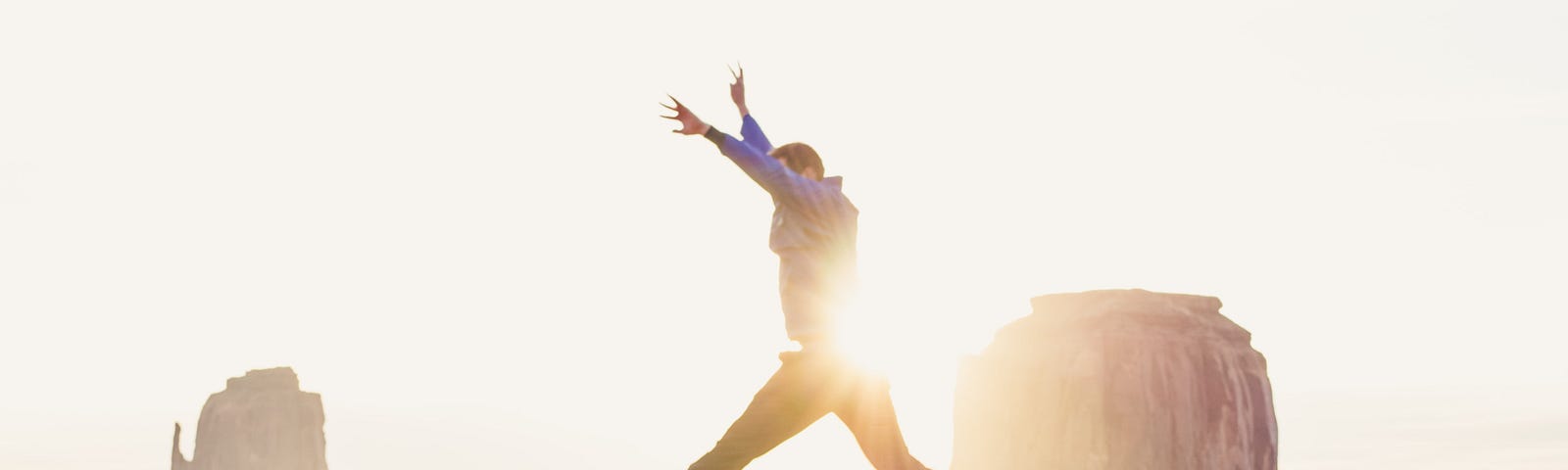 Man jumping over red rocks with sun shining