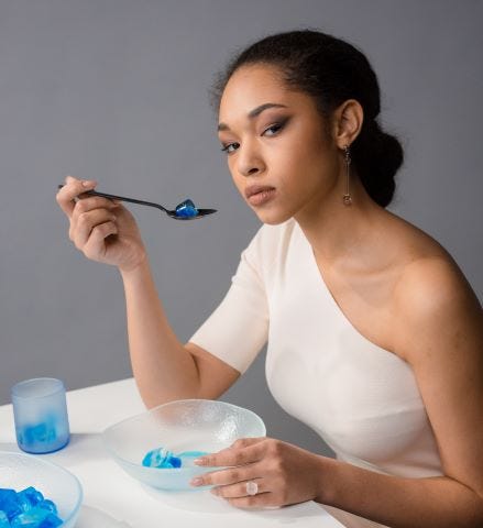 A woman is seated at a table eating what appears to be blue gelatin.