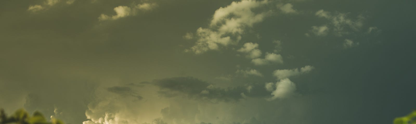 A woman stands with her head looking downward in a landscape photograph. Dark skies. Green hills.