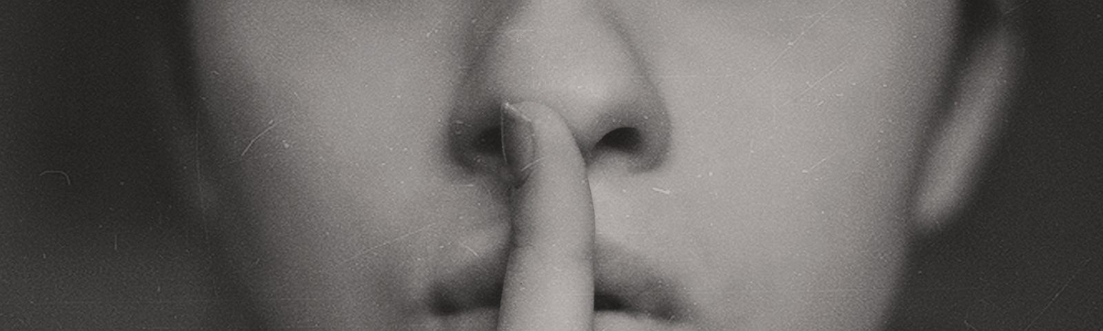 Woman presses her index finger to her lips requesting to be quiet