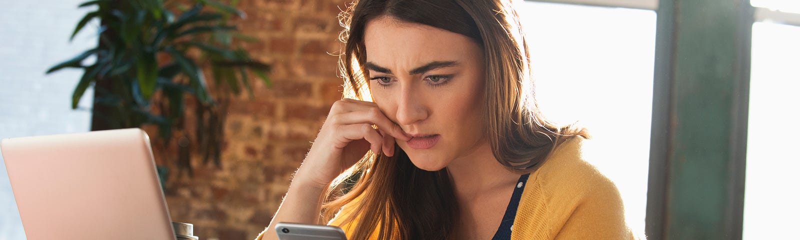 A stressed White woman biting her nails while looking at her cell phone.