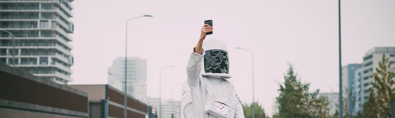 Person wearing astronaut standing in empty street with phone raised, taking a selfie.