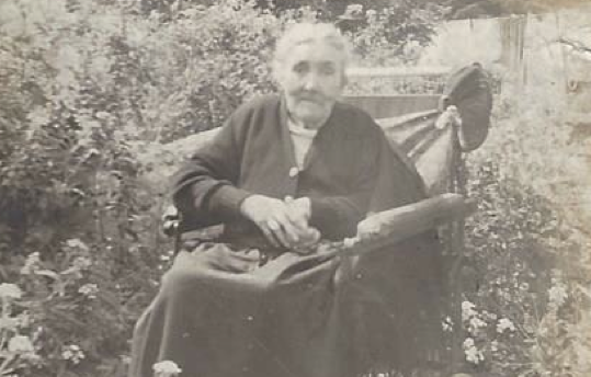 Old woman wearing a shawl, sitting in a wheelchair in a garden in Ireland, 1953.