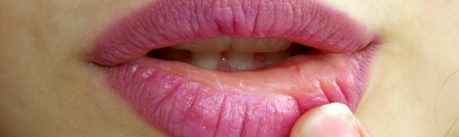 A portrait of a woman’s lips with a finger gently pulling on the bottom one.