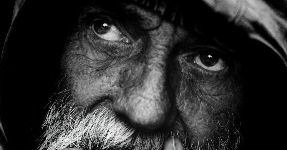 A close-up photo of an old man’s face with a grey moustache and beard. He is staring into the distance with a wondering expression focussing on something in the distance.