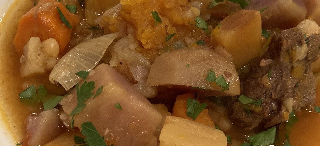 Shallow bowl of beef stew with large chunks of potato, garnished with chopped parsley.