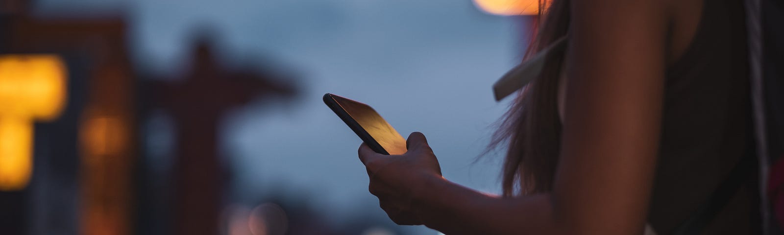 A photo of a woman looking at her phone at night on the street.