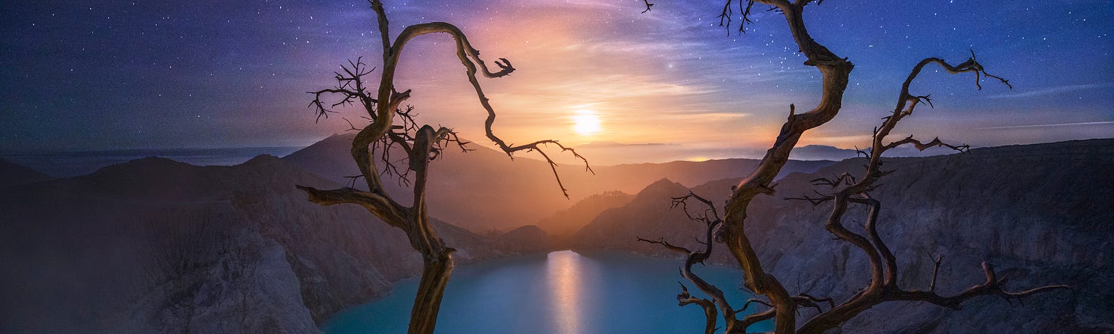 A fine art photograph of bare tree branches framing a moon and lake setting with purple clouds and stars