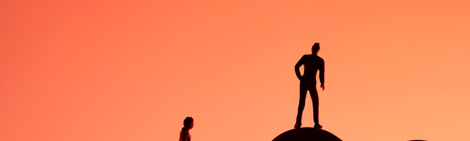 Silhouettes: A person sits on a large heart are the bottom lefthand corner of the photo; another person stands on another large heart in the bottom righthand corner. The black silhouettes are set off by a pinkish/salmon background.
