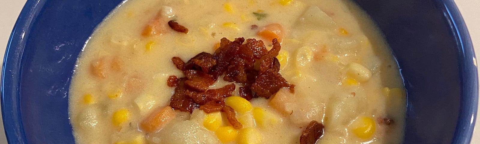 A blue ceramic bowl filled with corn chowder that’s topped with crumbled bacon.