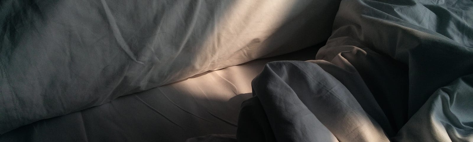 A photo of an empty bed. White pillows, bedsheets. A strand of light adds some warmth to the center.