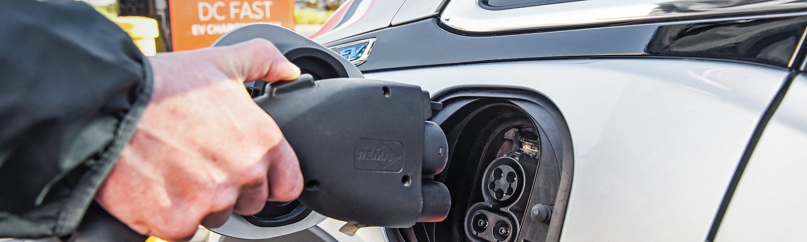 A hand plugging an electric car in to charge.