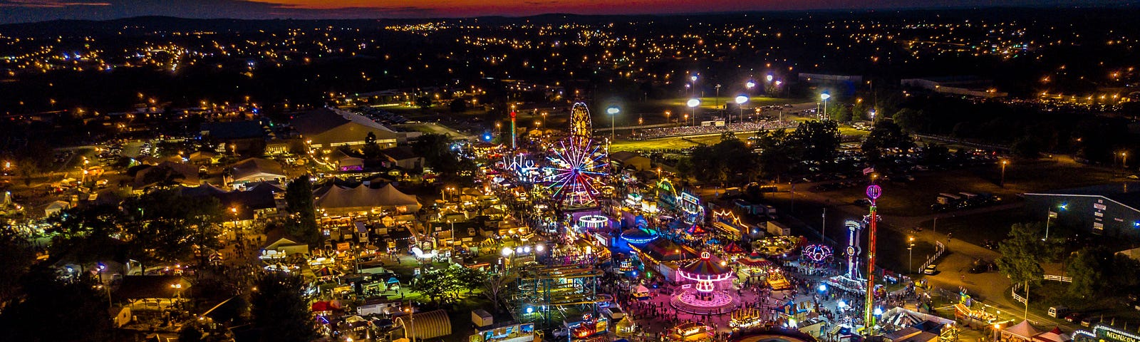 Night-time carnival lit up in colorful lights with the sun setting.