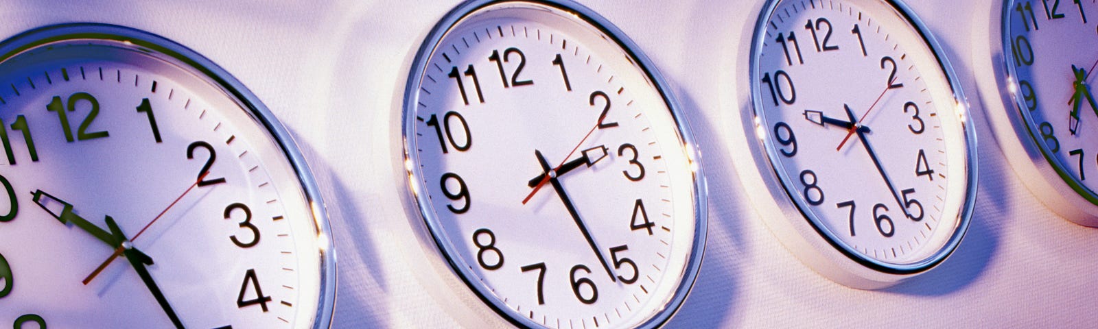 Four office clocks in a row, all portraying different times.