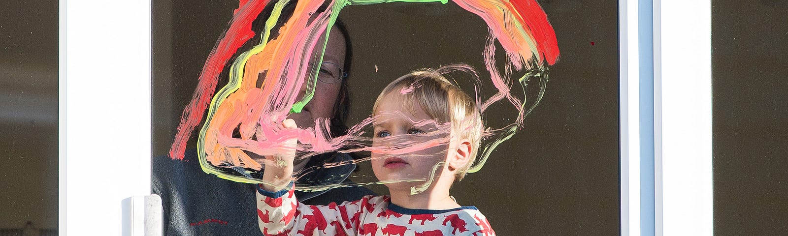 Together with his mother, a boy paints a rainbow on the window of their apartment.