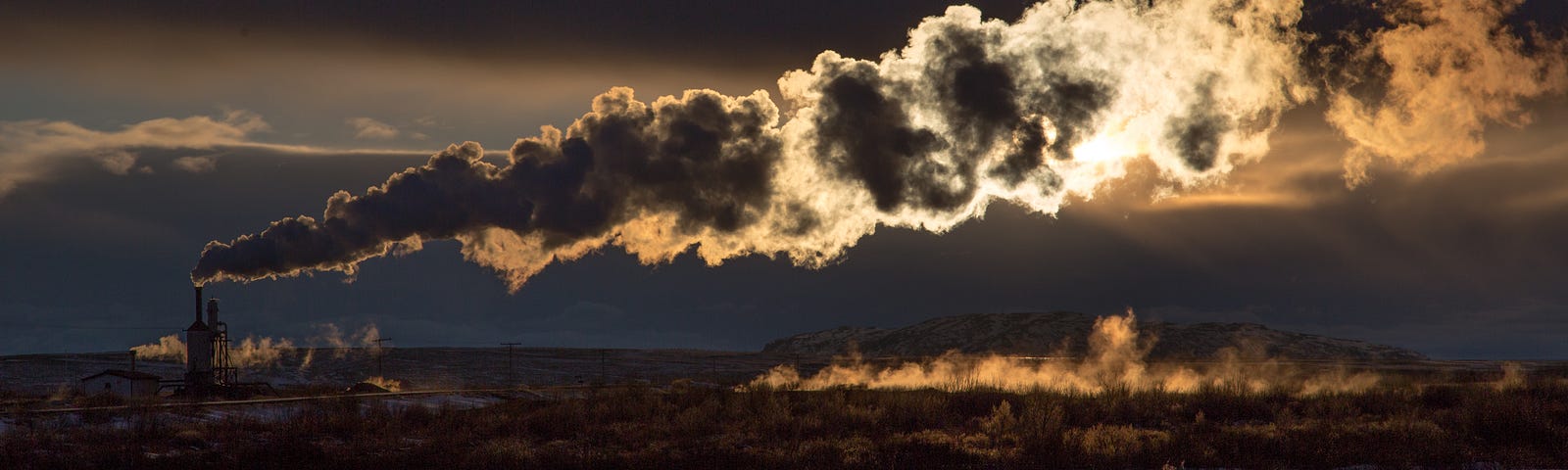 A factory exhaust pipe emits smoke over the land. The sun peers through the clouds of smoke.