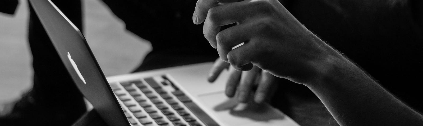 Black and white photo of a person on their laptop, face obscured.