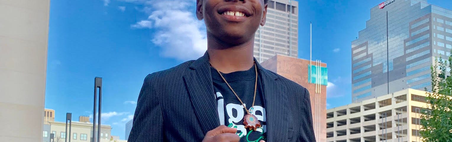 Te’Lario Watkins II smiling and posing in front of tall buildings and a bright blue sky.