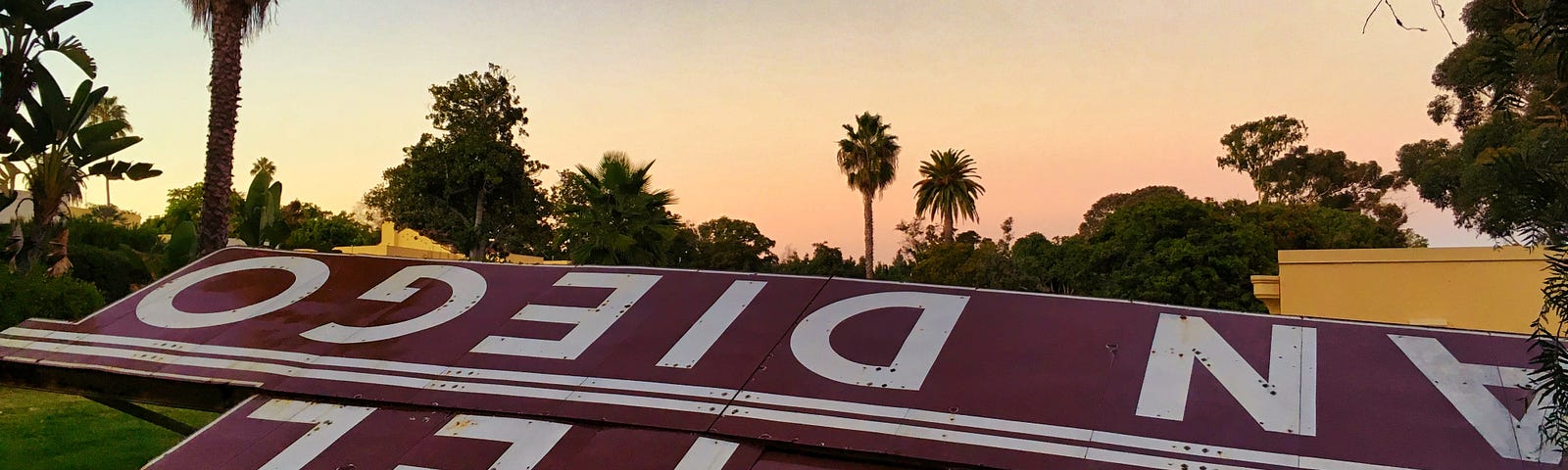 A vintage Hotel San Diego sign lays on the ground with a sunset and palm trees in the background