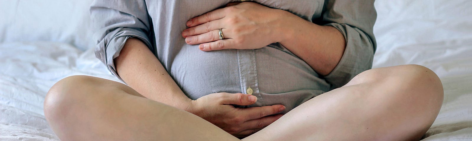 A pregnant woman sits on her bed.