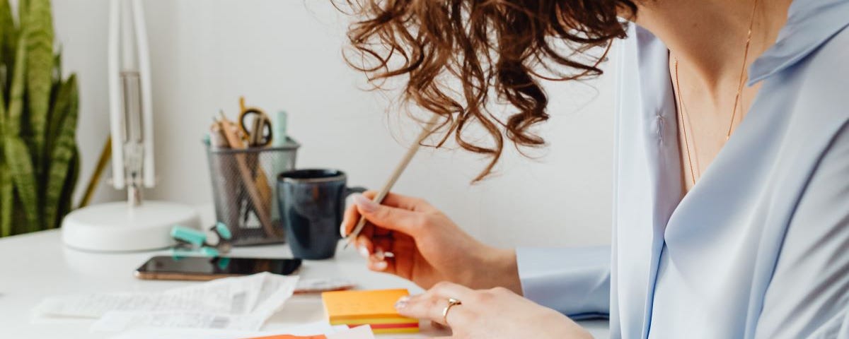 A young woman works on her finances with a pencil, sticky notes, forms, and a calculator.