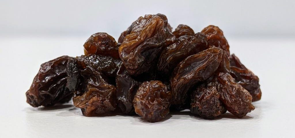 A close-up of a small mound of raisins on a white table with a white background.