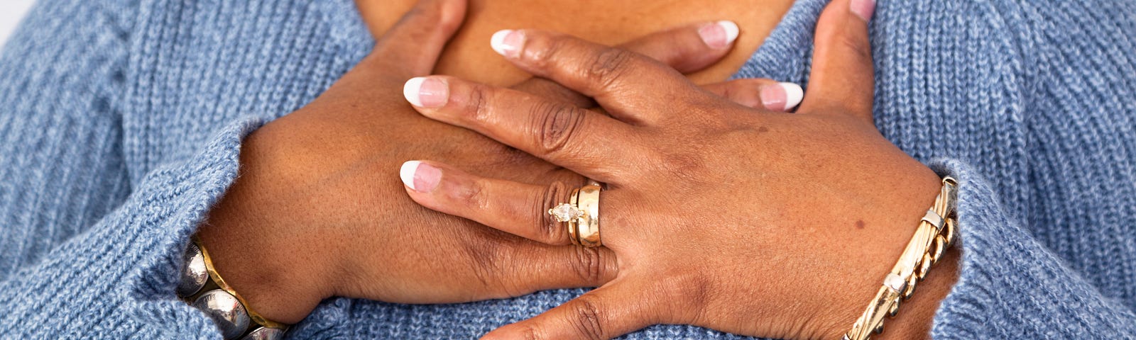 A close-up photo of a woman clasping her hands over her chest.