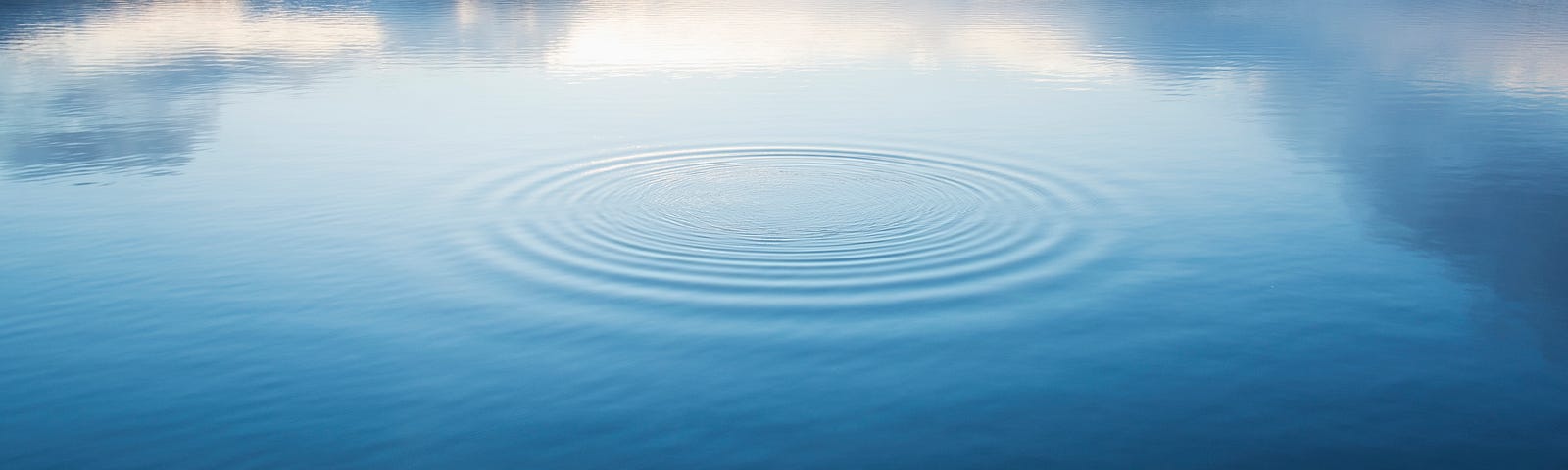 A singular circular pattern ripples on a calm lake’s surface.