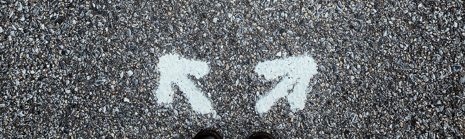 Two shoes on an empty street, each facing an arrow pointing in opposite directions