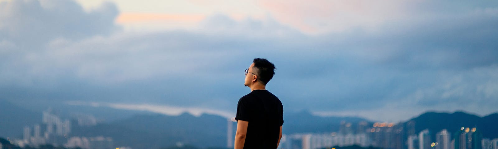 A man looks out at the sky and cityscape.