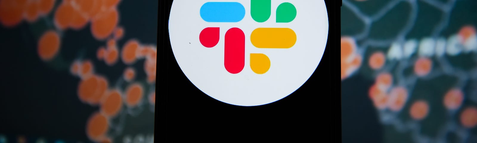 In this photo illustration a Slack logo seen displayed on a phone with a World map of COVID 19 epidemic on the background.